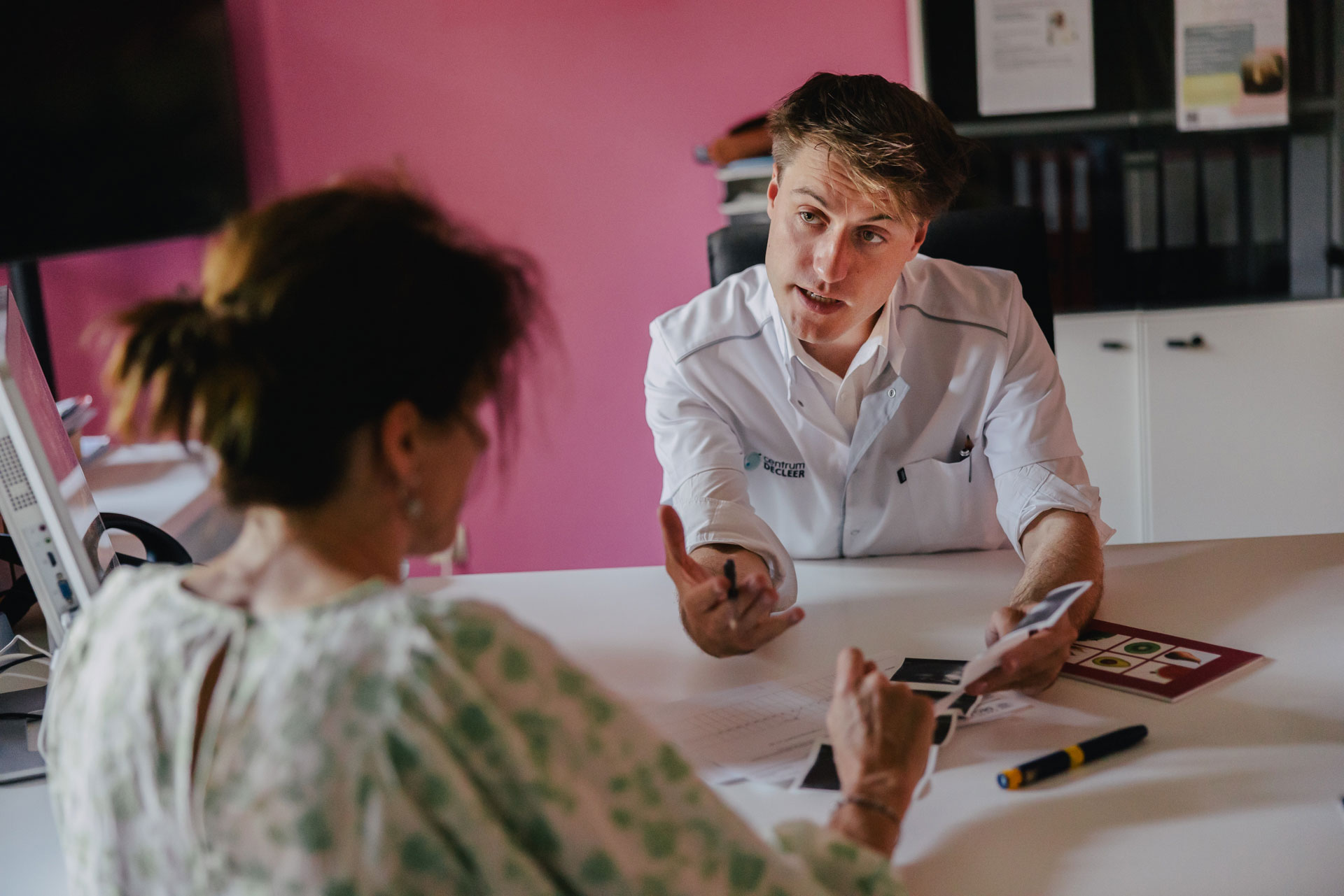 Arts in witte jas bespreekt chirurgie met patiënt aan bureau.