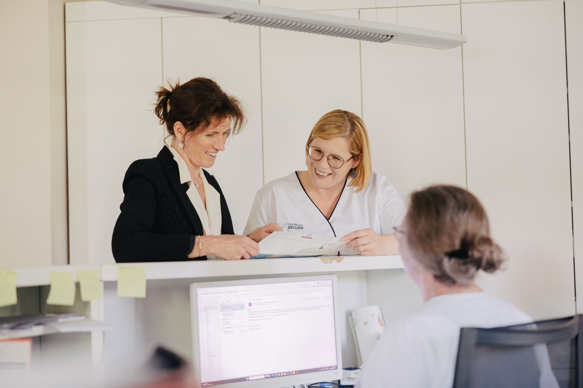 Twee lachende vrouwen bij de balie, mogelijk over intra-uteriene inseminatie (IUI) documenten.