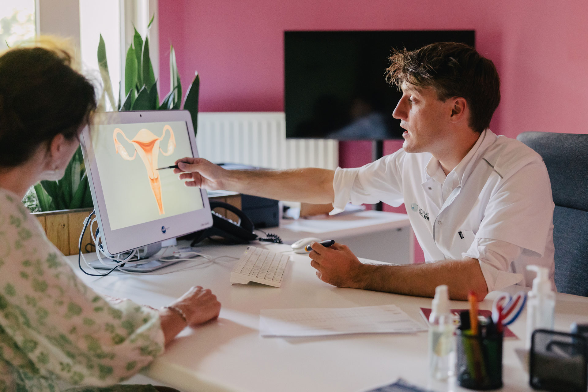 Arts legt IUI-procedure uit aan patiënt met afbeelding van de baarmoeder op een computerscherm.