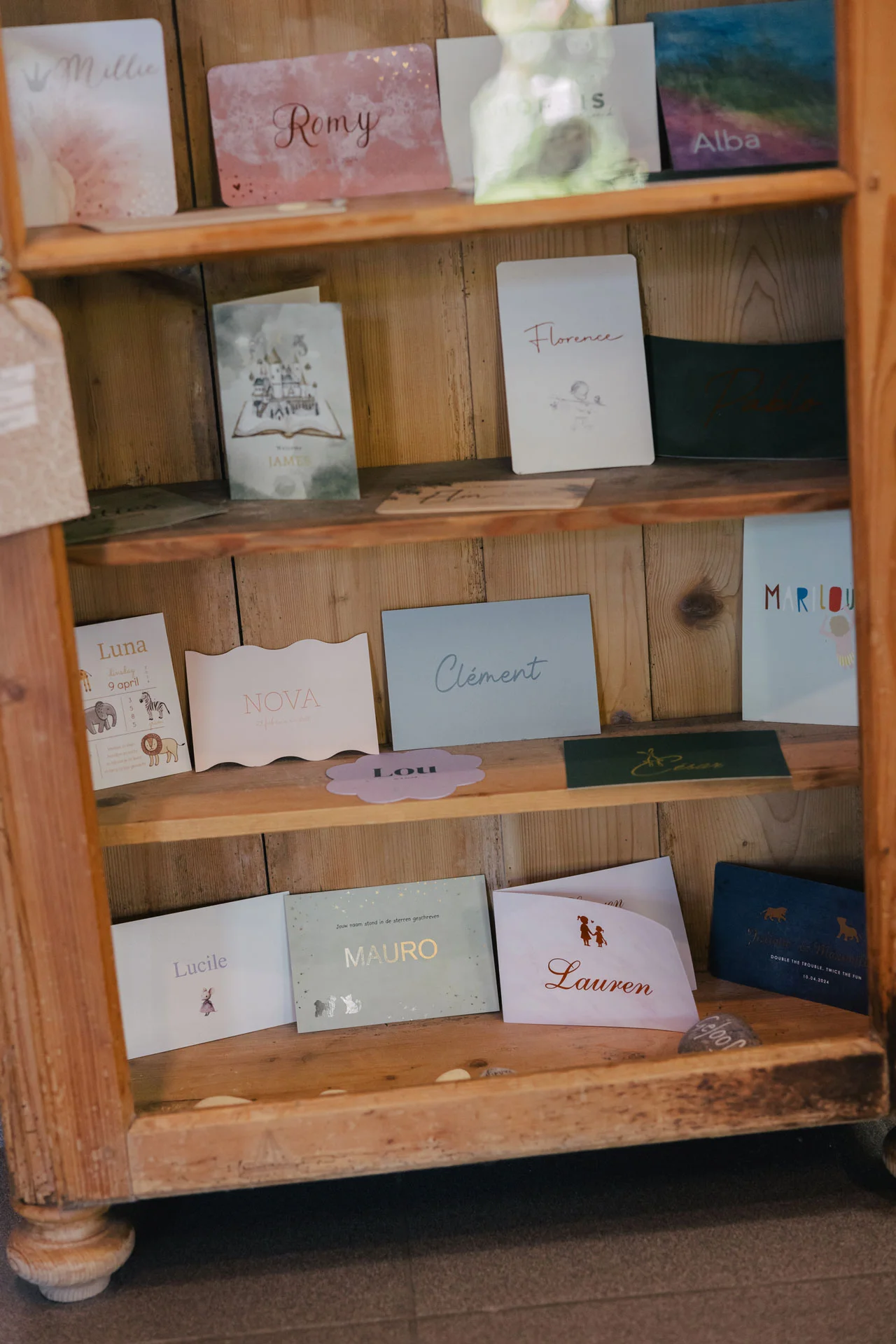 Houten kast met naamkaartjes, waaronder 'Millie', 'Romy', 'James' en 'Lauren'.