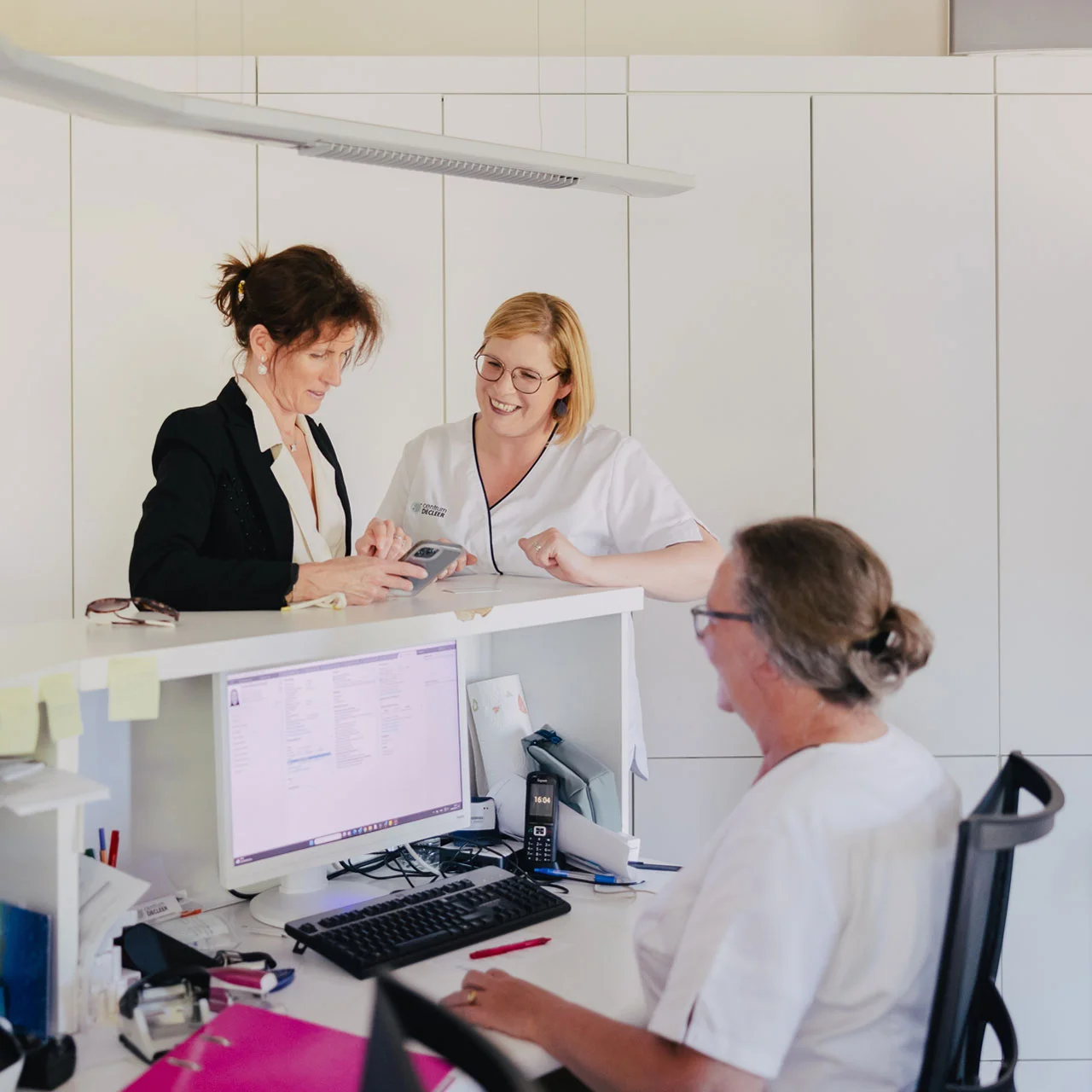 Over ons: Vriendelijke medewerkers bij de receptie van een dokterspraktijk in gesprek.