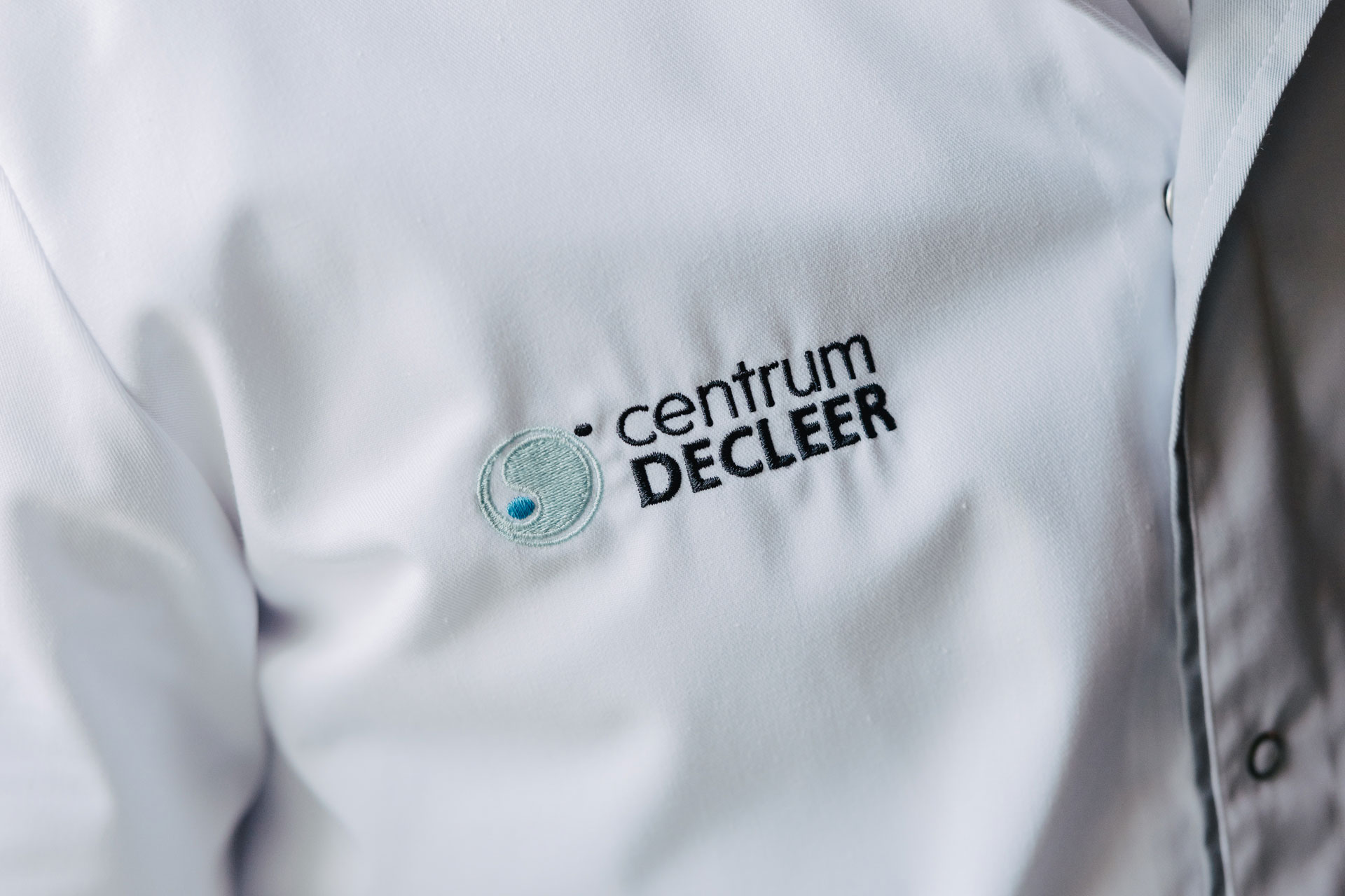 Geborduurde logo "Centrum DE CLEER" op een witte doktersjas.